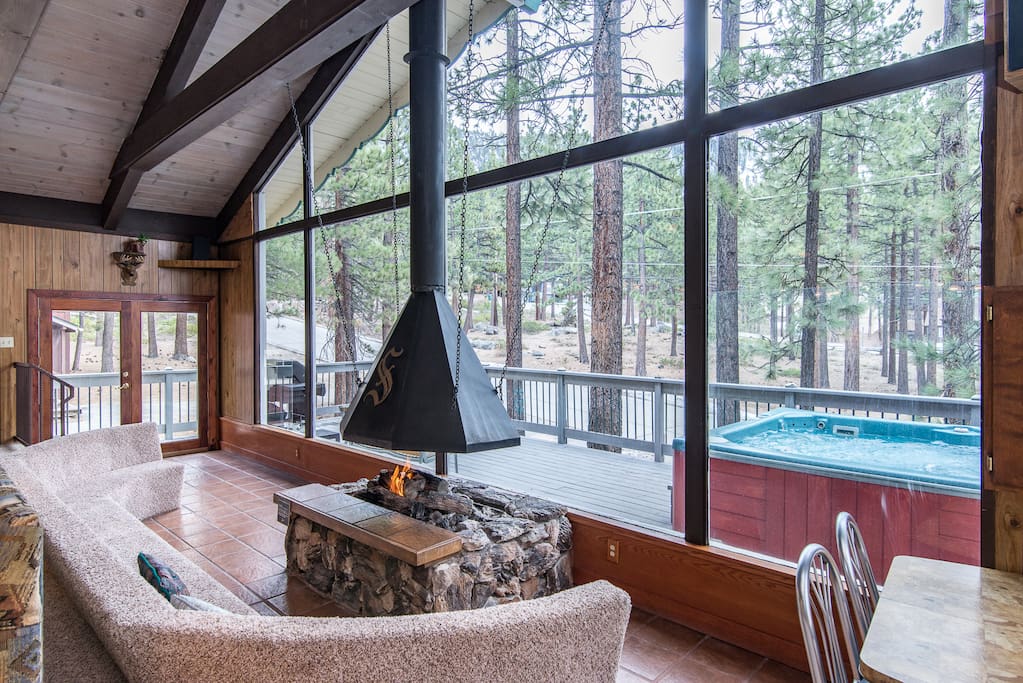 A huge seating area sits before an open stone fireplace and stunning floor-to-ceiling windows.