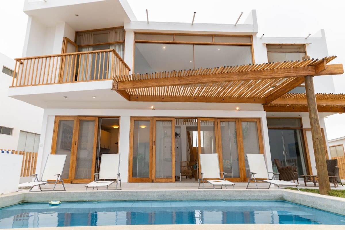 The exterior view of the house features a spacious wooden deck with lounge chairs alongside a private pool. Large sliding glass doors provide a connection between outdoor and indoor spaces, enhancing the inviting atmosphere of the home.