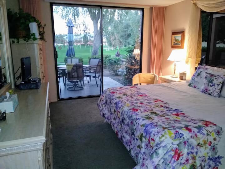 Главна спална соба (отворени нијанси) со поглед на задниот двор и теренот за голф, мал телевизор во спалната соба