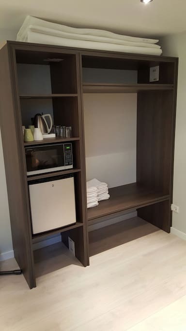 Open cupboard with minifridge, microwave watercooker, tea and coffee