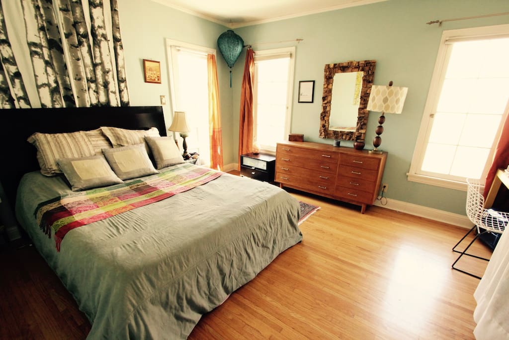 Sunny quiet aqua bedroom with garden and lower patio access, comfortable queen bed, both shades & curtains, wardrobe & dresser space, and a desk with Harry Bertoia chair.