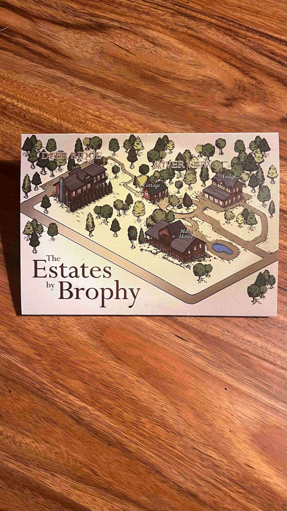 A detailed illustrated map of The Estates by Brophy is presented. It features various buildings, paths, and a pond, surrounded by trees. The layout is designed to guide visitors through the property, highlighting key locations and amenities.