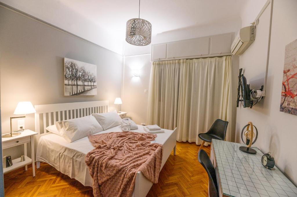 A cozy bedroom showcases a spacious bed dressed in light linens and accompanied by soft, textured blankets. Bedside lamps provide gentle lighting, and light-colored curtains frame a window. A desk with a patterned surface is positioned next to the bed, enhancing the room's functionality.