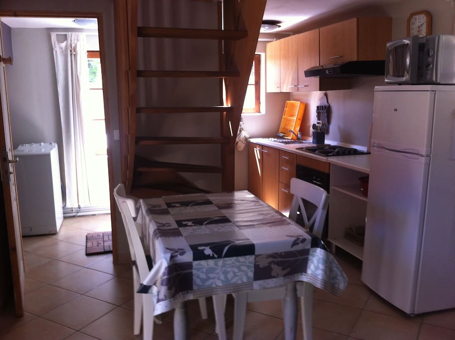 Coin repas donnant sur la cuisine équipée (frigo, congélateur, micro ondes, four, 4 plaques électriques).