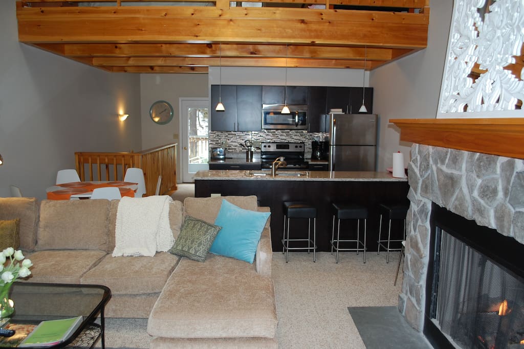 Great room looking into full kitchen with counter stools. Loft above.