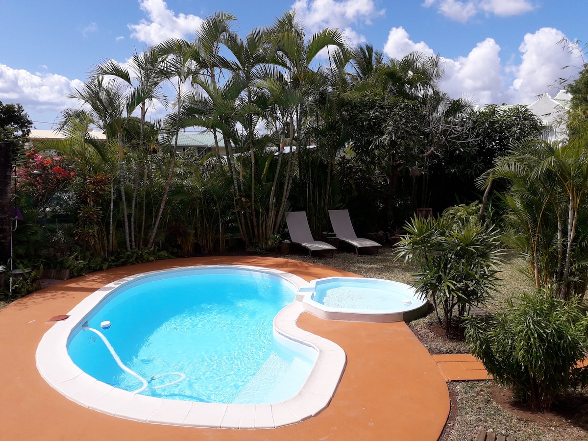 A private pool is set in a well-maintained garden surrounded by lush greenery. Two loungers are positioned beside the pool, inviting relaxation under the sun. The distinct contours of the pool and its attached area add a unique touch to the outdoor space.
