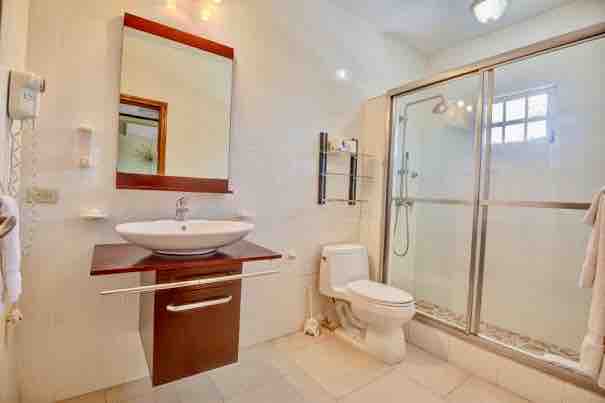 A modern bathroom is equipped with a glass-enclosed shower and a sleek vanity featuring a round sink. A large mirror above the sink enhances the space, while soft lighting complements the neutral tile floor and walls.