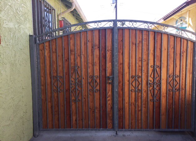 A sturdy wooden gate with metal accents stands closed, providing an inviting entrance. The gate features decorative designs and is flanked by textured wall surfaces. A sense of privacy is offered, reflecting the secured nature of the property.