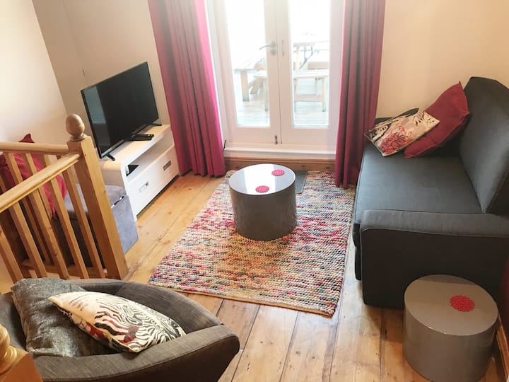 סלון בקומה 2 עם ספה ושולחן גבוה עם שרפרפים, המוביל למרפסת השמש. חדר מואר ומאוורר ונעים בלילות החורף.