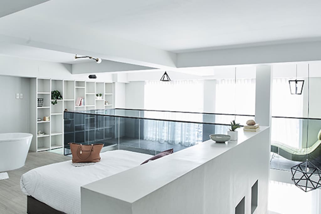 Compared to other lofts that look a bit tight and cramped, this one is open, spacious, and airy. A glass railing keeps the area safe while defining the spaces within the loft. Meanwhile, the topmost part of the shelf can be seen from the sleeping area. And yes, the bathtub sits at the foot of the bed!