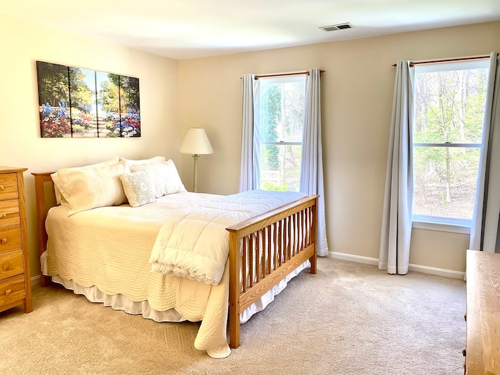 This spacious bedroom suite has one queen sized bed, suitable for two people, and a private bathroom with double sinks. Two large windows provide light and  a view of the back yard woods. 