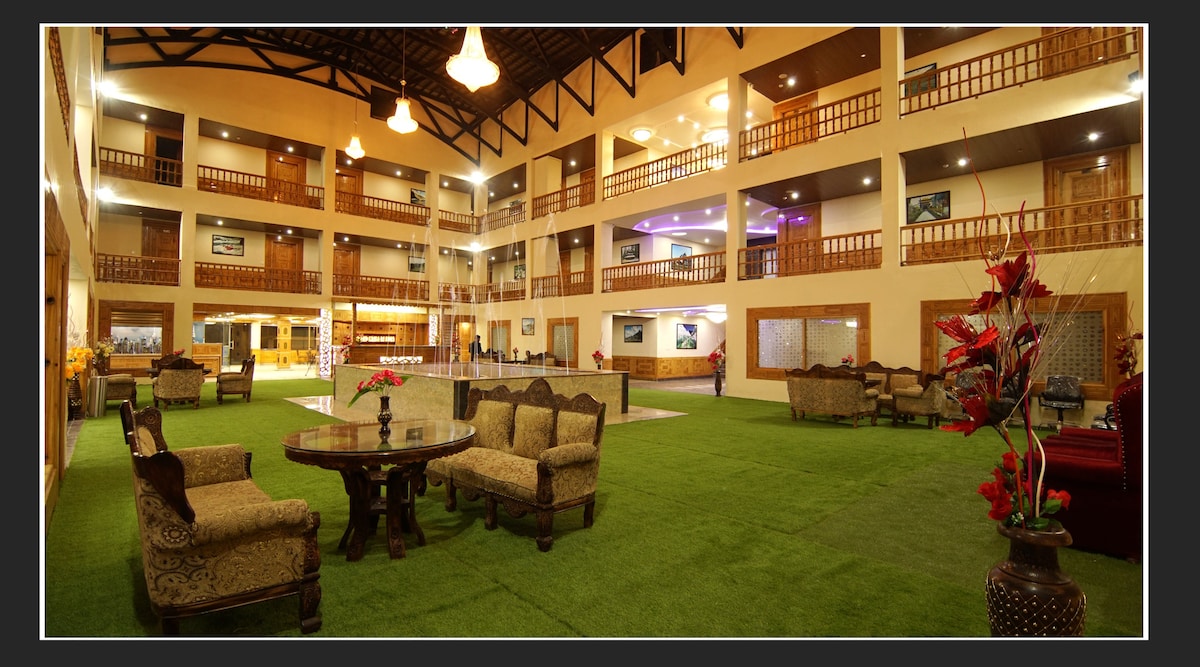 A spacious lobby area is displayed, featuring well-arranged seating with ornate chairs and tables. The indoor greenery creates a refreshing atmosphere, while overhead lighting adds warmth. Multiple levels of balconies overlook the space, enhancing the airy and open feel.