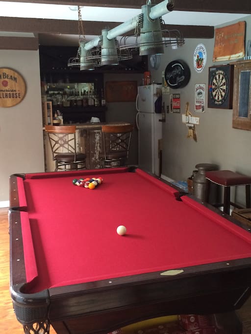 Play pool and darts, while watching the pregame shows and lounging at the bar. A sliding glass door to the left looks outside at the pool, a firepit, and smoker, and a ping pong table.
