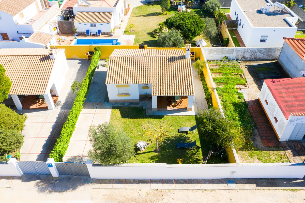 The image depicts a spacious outdoor area surrounding two houses. Green lawns are filled with trees, and a pathway leads to a patio with seating. The roofs of the houses are tiled, and neighboring properties show additional gardens, creating a tranquil and inviting ambiance.