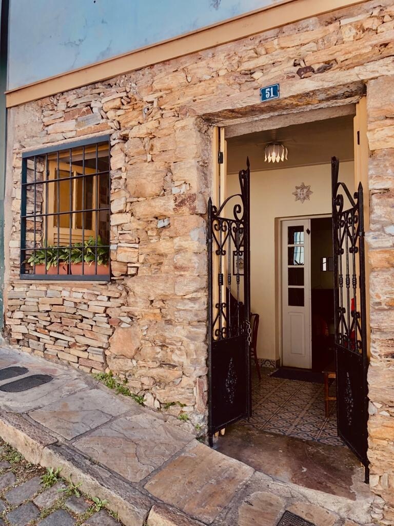 The entrance features a sturdy wrought iron gate, set against a rustic stone facade. Soft light filters through a decorative lamp, illuminating a welcoming hallway that leads into the kitinet, enhancing a sense of warmth and security.