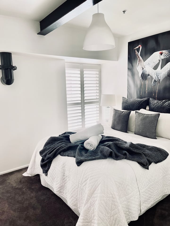 Cama tamaño queen con batas integradas y ventanas del piso al techo con persianas de plantación.