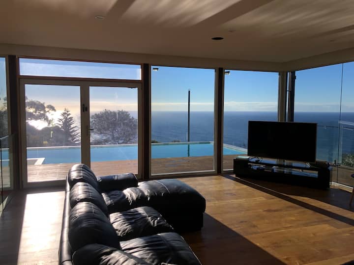 客厅可直接通往泳池和海洋甲板，四周环绕着泳池、灌木丛和海景