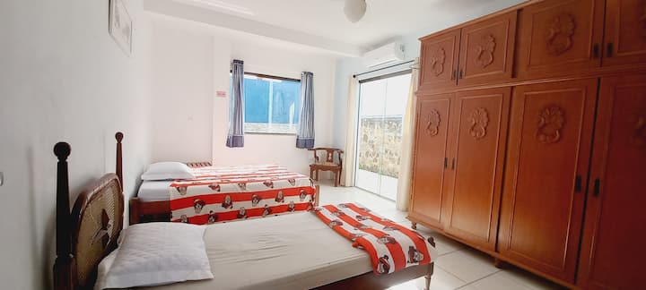 غرفة في الطابق الأرضي مع مكيف هواء ومروحة سقف وأسرّة مزدوجة وأسرّة مفردة. تهوية جيدة جدًا، ولها مخرج إلى المنطقة الخارجية.