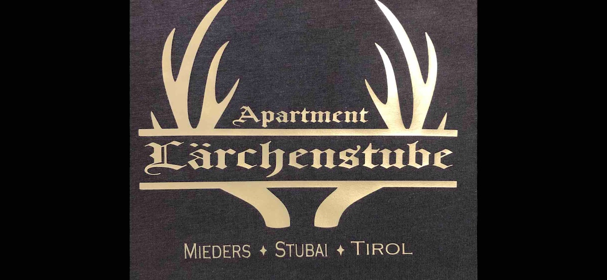The entrance sign for Apartment Lärchenstube features a stylized design with antler motifs. The name of the apartment is elegantly displayed in a bold font, accompanied by the location details: Mieders, Stubai, and Tirol, all presented in a contrasting color against a dark background.