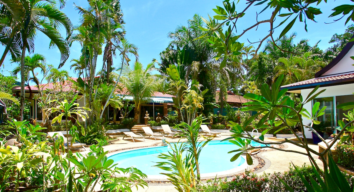 A well-maintained pool area is surrounded by lush tropical plants and palm trees. Comfortable lounge chairs are positioned near the inviting pool, creating a serene outdoor escape. The vibrant greenery enhances the sense of privacy and tranquility in this inviting space.