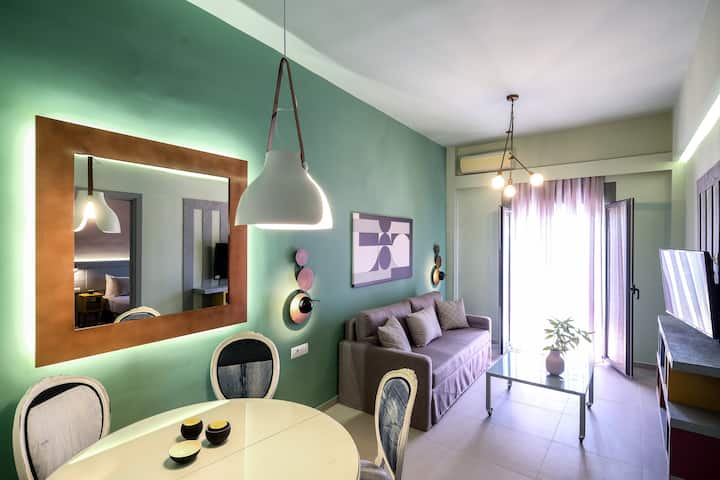 apt. 27-103, sala de estar com sofá-cama e área de jantar para 4 pessoas.