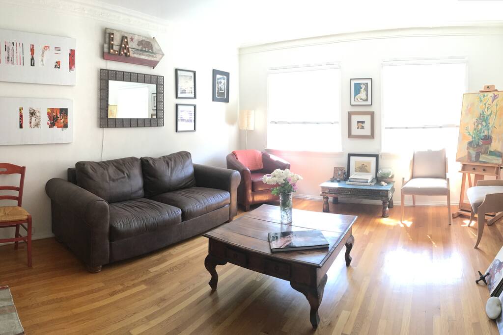 Large and inviting Living Room features a leather sofa and meditation chair, two big windows open to an expansive view of the Hollywood Hills and garden below. Fine art and photography curated through out.