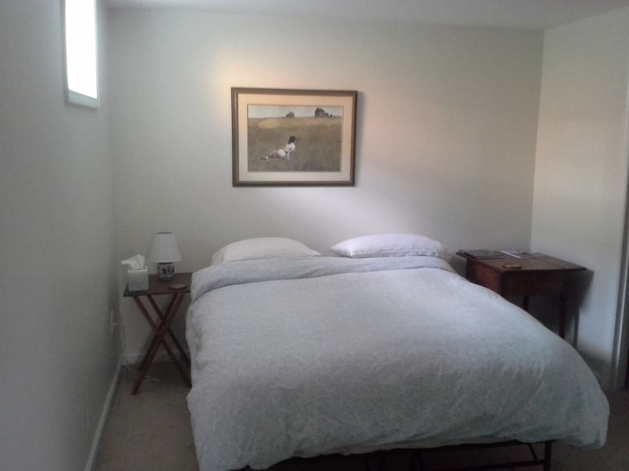 Comfortable queen bed with pillow top mattress in clean, sunny bedroom.