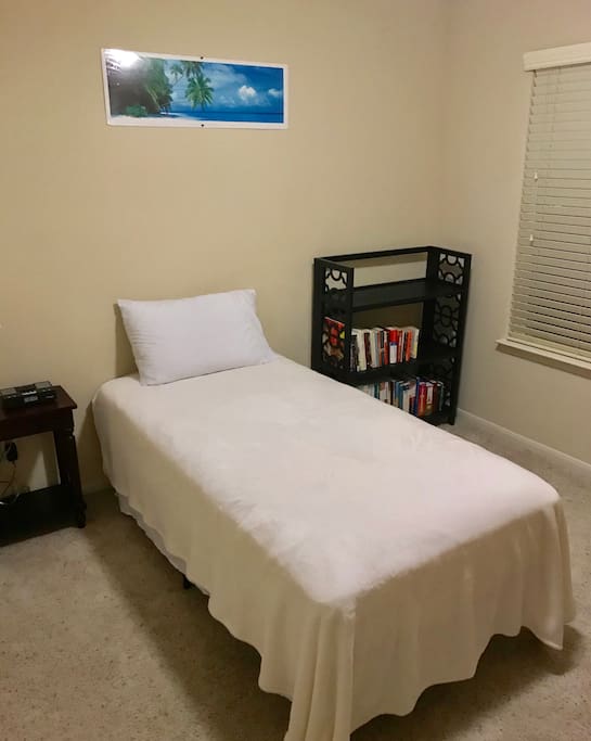 Cozy bedroom with twin sized bed, alarm clock, and bedside table.