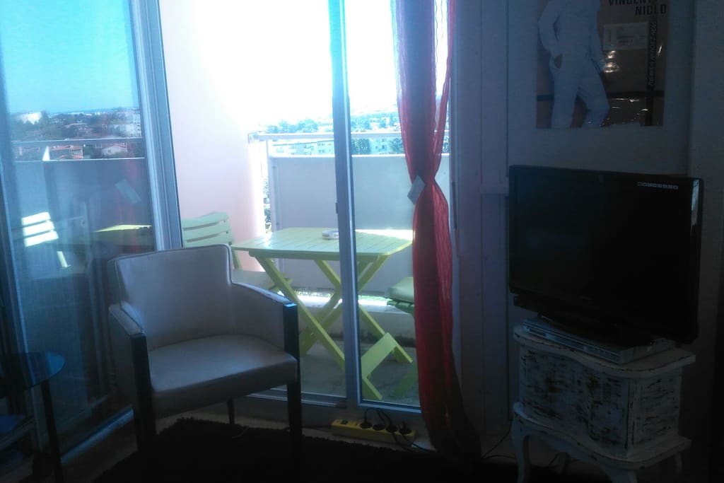 fauteuil et TV dans la chambre privatif avec table et chaises sur le balcon vue sur Toulouse.