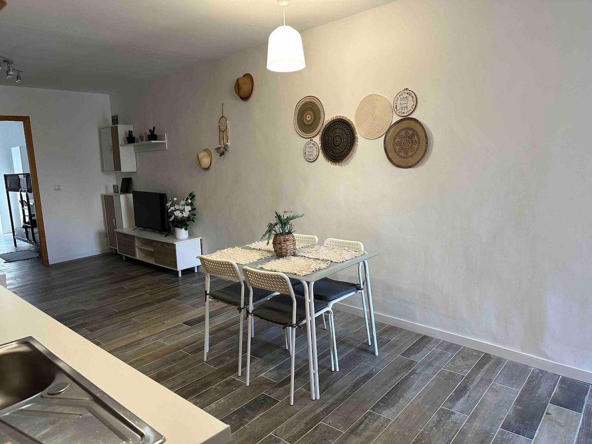 A dining area is visible, featuring a light-colored table surrounded by four chairs. Various decorative plates are arranged on the wall, adding character to the space. Neutral tones and natural lighting create a calm atmosphere, enhancing the inviting feel of the open layout.