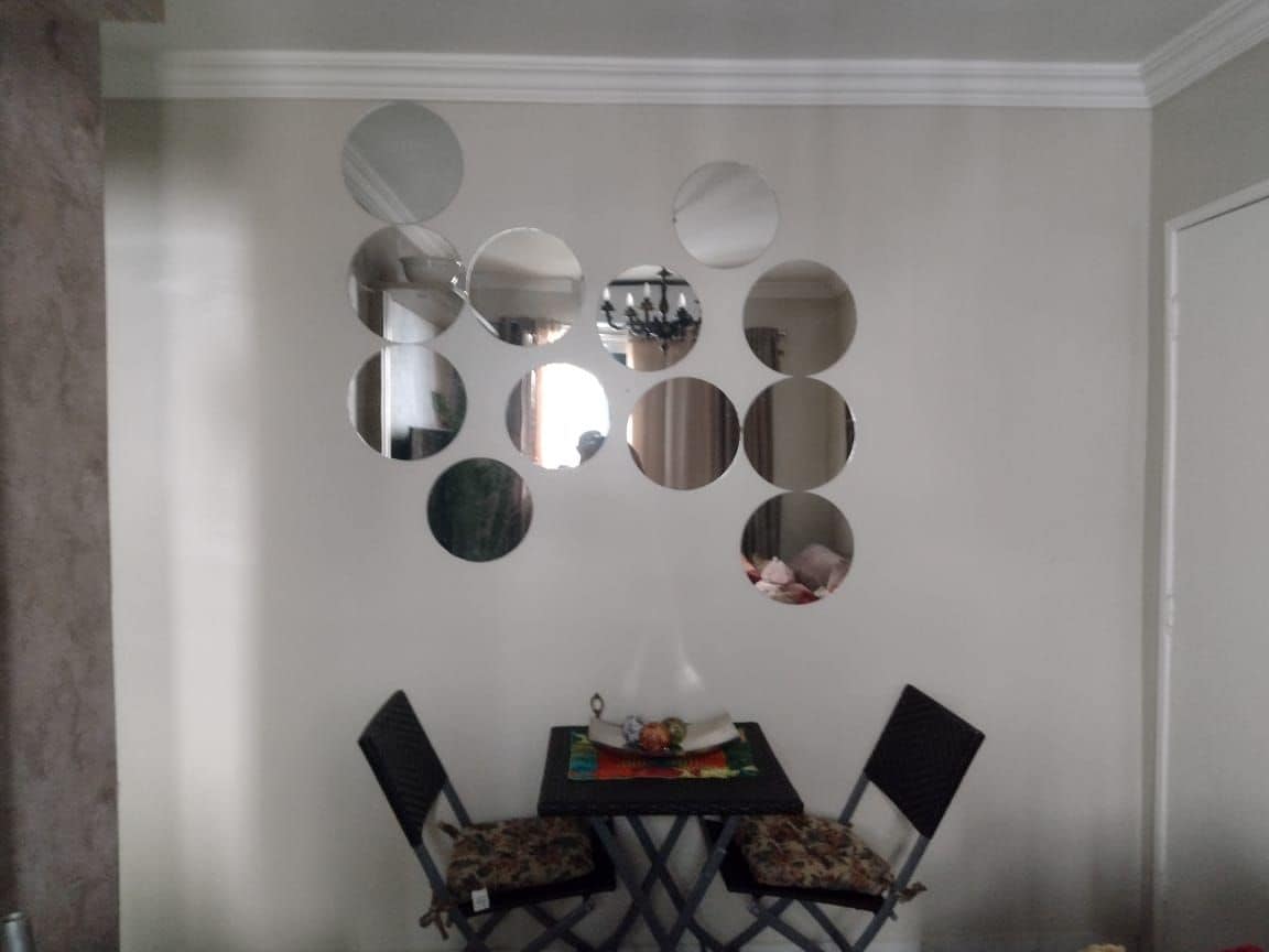 A dining area is featured, showcasing a small table paired with two chairs. A decorative arrangement of round mirrors is mounted on the wall, reflecting light and adding depth to the space. A centerpiece of fruit is displayed on the table.