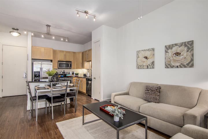 Kitchen and Living room features sleek granite counters, stainless appliances, track lighting, and a neutral color palette with hardwood-style floors.