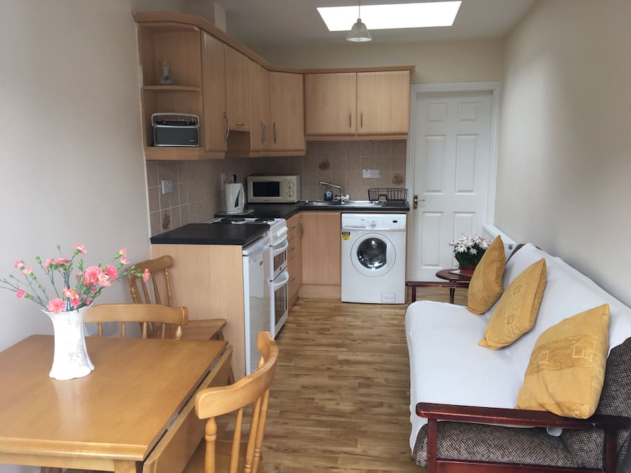 Kitchen with washing machine & dryer, sofa, table and three chairs.