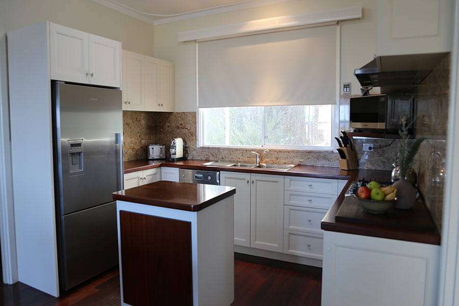 A modern kitchen is equipped with stainless steel appliances and a spacious island. Natural light filters through a large window, illuminating the wooden countertops and cabinetry. Essential kitchen items, including a microwave and coffee maker, are neatly arranged for easy access.