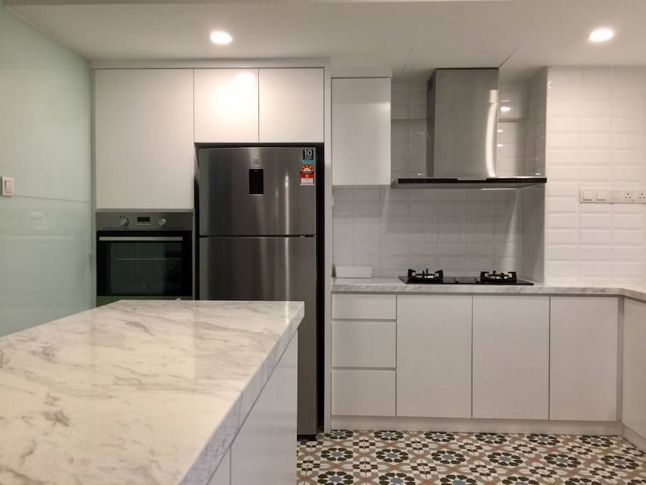 A total white Open kitchen with gas stove, oven n fridge. The kitchen is also equipped with pots, pans and cooking utensils.