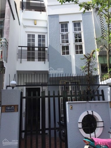 The exterior of the property is showcased, featuring a modern design with large windows and a light-colored facade. A gated entrance leads to a welcoming pathway. Decorative elements include black railings and a circular window, adding character to the entrance.