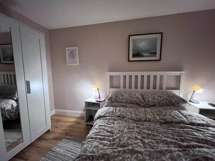 Dormitorio amplio y luminoso con una cómoda cama tamaño king, armario con estantes y mesita de noche. El dormitorio tiene una vista parcial al mar.