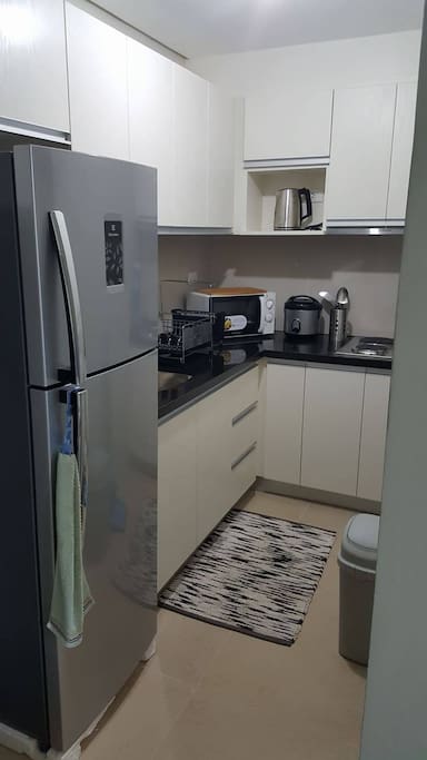 Furnished kitchen with electric stove, exhaust fan, rice cooker, microwave oven, electric kettle, cooking wares, plates, and utensils.