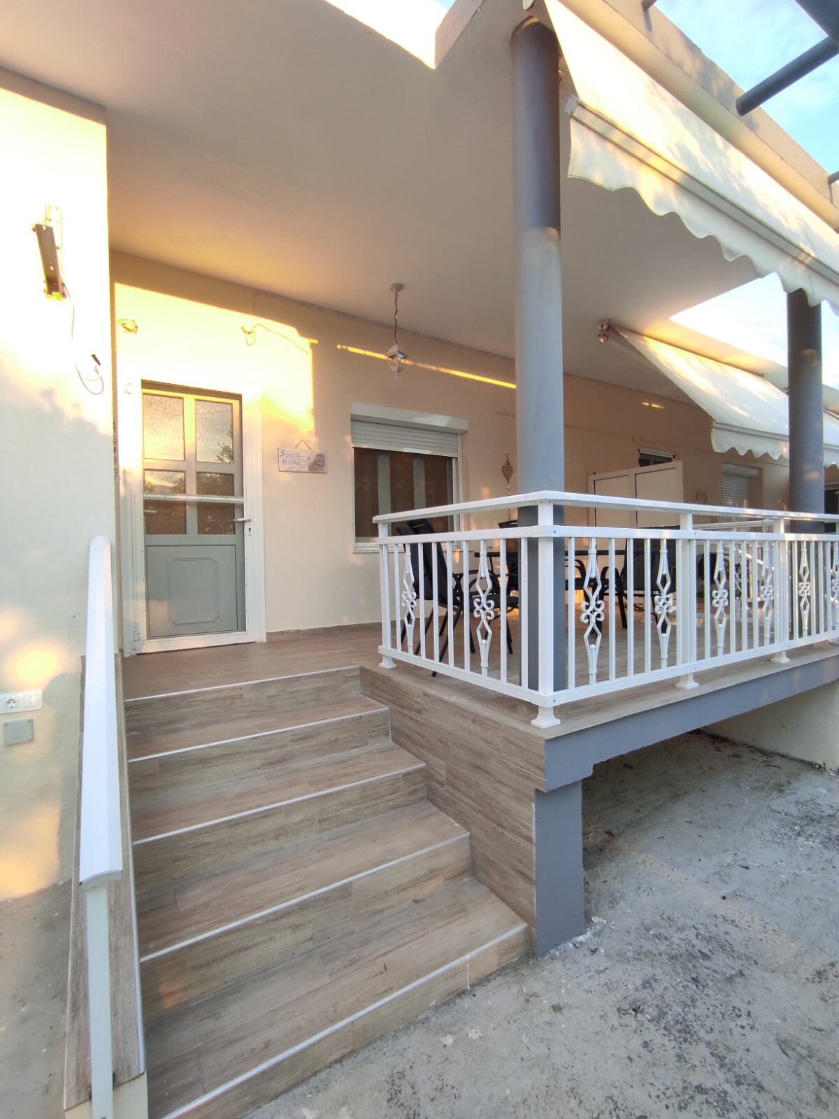 A welcoming entrance is visible, featuring a set of stairs that lead to a covered porch. The porch is adorned with a railing and provides access to a door framed by large windows. Soft lighting enhances the entryway’s inviting look.