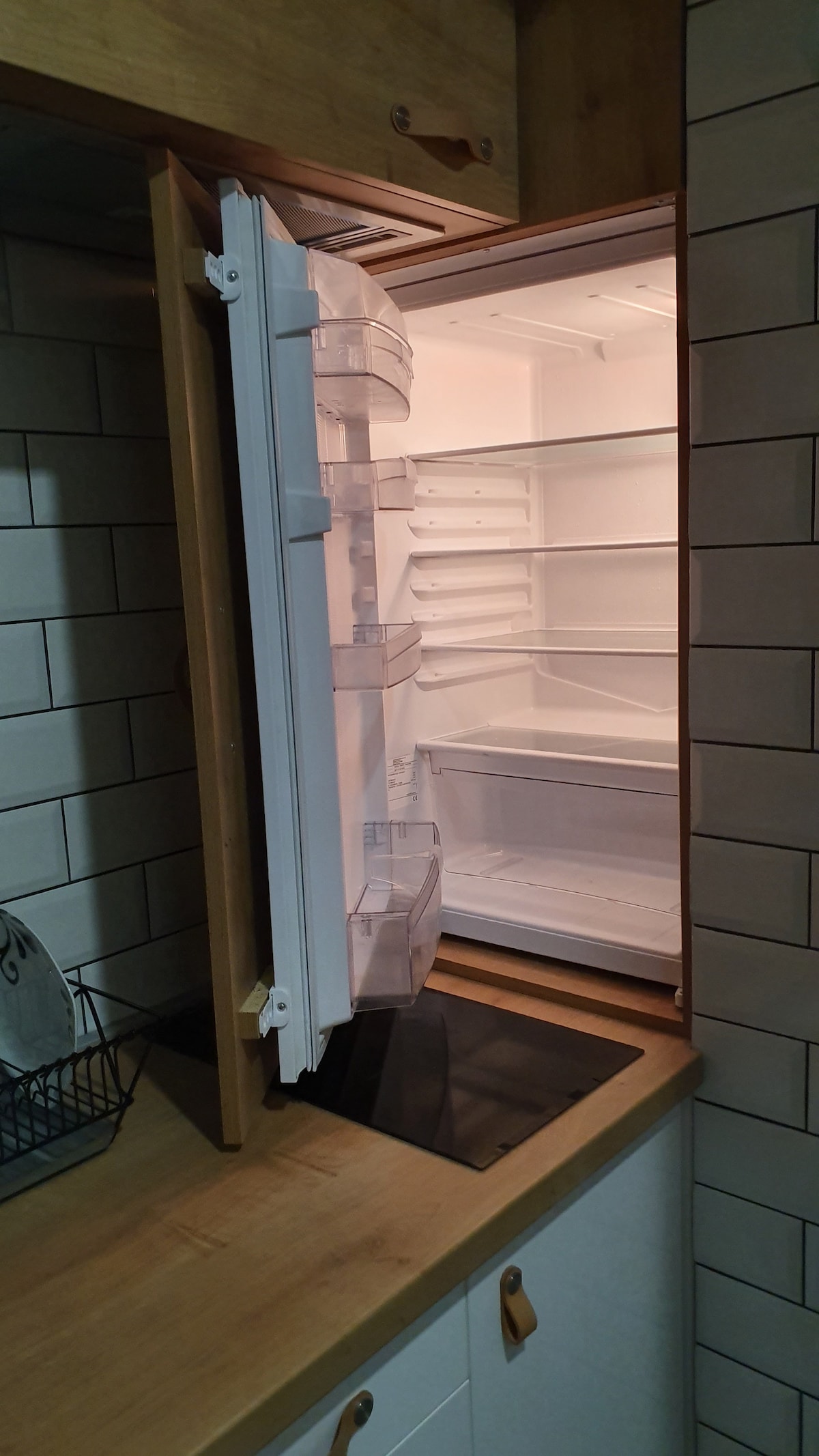 A spacious refrigerator is shown with its door open, revealing clean, empty shelves and compartments. The interior lighting is bright and the fridge is well-maintained, featuring a minimalist design that complements the surrounding kitchen space.