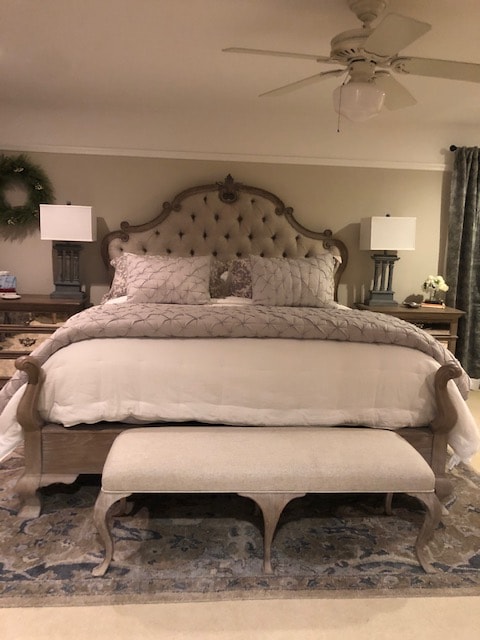 A spacious bed is centered against an elaborately designed headboard, featuring soft bedding with subtle patterns. Two bedside lamps provide soft lighting, while a decorative bench sits at the foot of the bed. A patterned area rug enhances the warmth of the room.