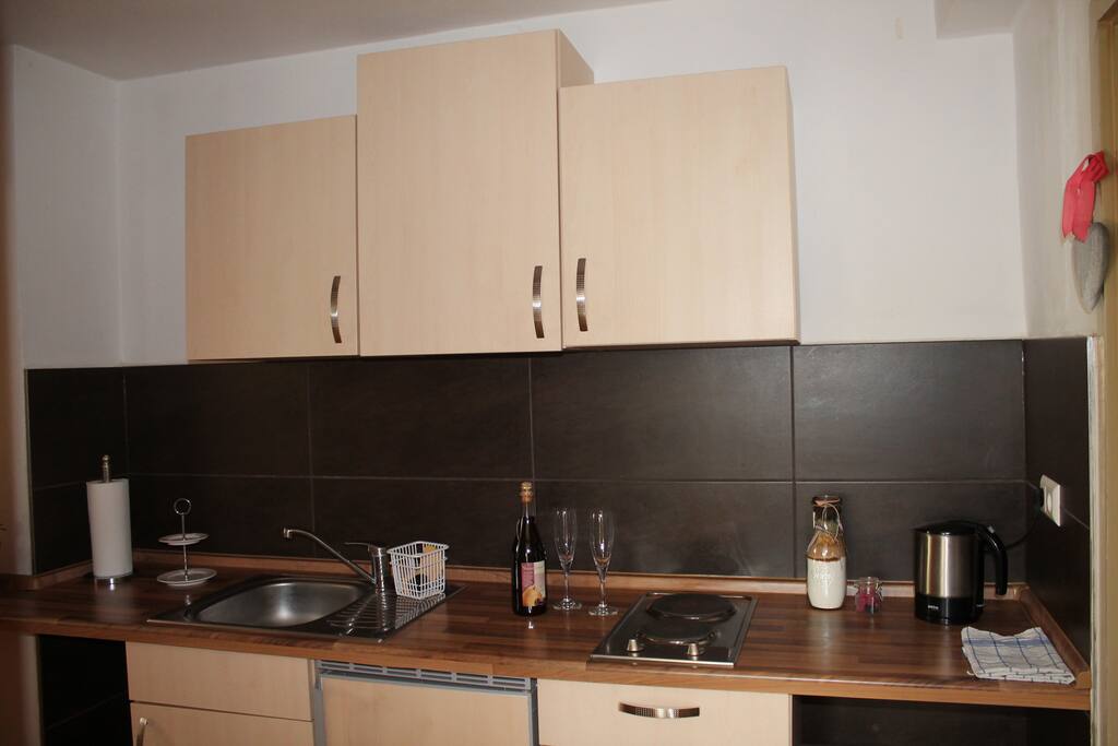 Küchenzeile mit zwei Herdplatten, Wasserkocher und Kühlschrank mit kleinem Gefrierfach.