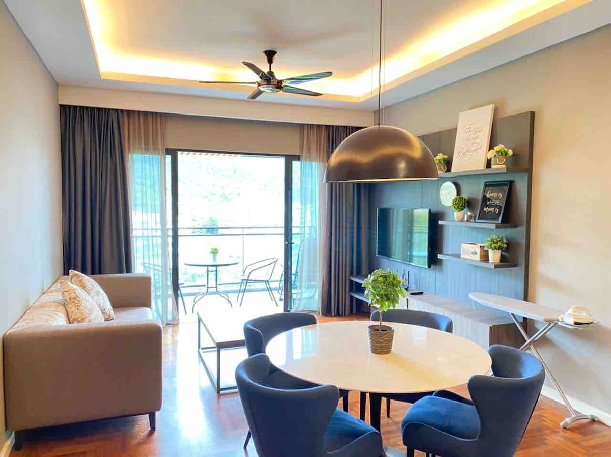 An inviting living area features a modern sofa and a round dining table surrounded by blue chairs. A sleek ceiling fan provides air circulation. Natural light brightens the space, streaming in through large glass doors that open to a balcony with outdoor seating.