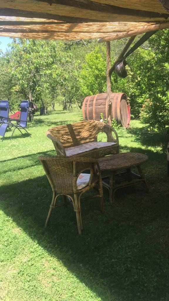 A serene outdoor space is shown, featuring a small table and two wicker chairs placed on a grassy area. Two lounge chairs in the background invite relaxation, while a wooden barrel adds a rustic touch to the garden setting.