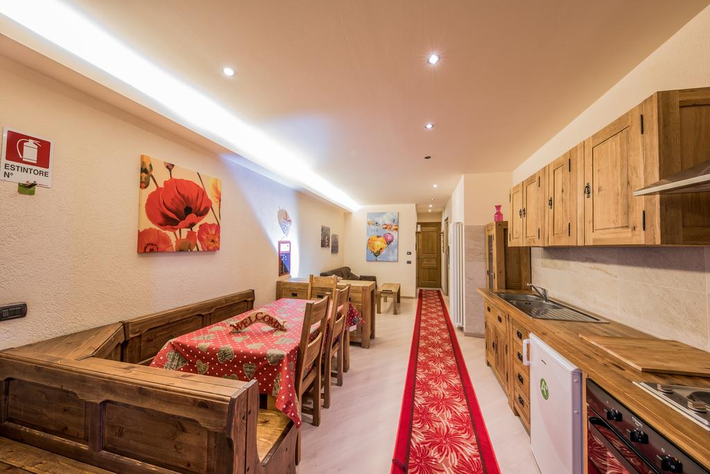 The dining area is furnished with wooden tables and chairs, set with colorful tablecloths. The kitchen features wooden cabinets and modern appliances. Decorative artwork adorns the walls, enhancing the warm and welcoming ambiance of the open space.