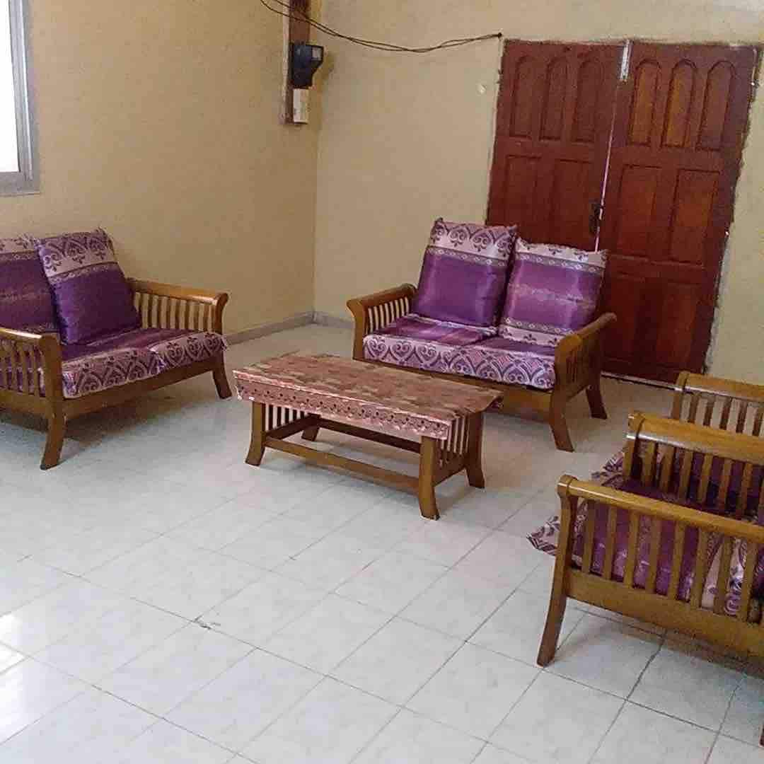 A spacious living area is presented featuring wooden seating with vibrant purple cushions. A rectangular wooden coffee table occupies the center, while two sets of twin doors provide access to the outside, enhancing the openness of the space.