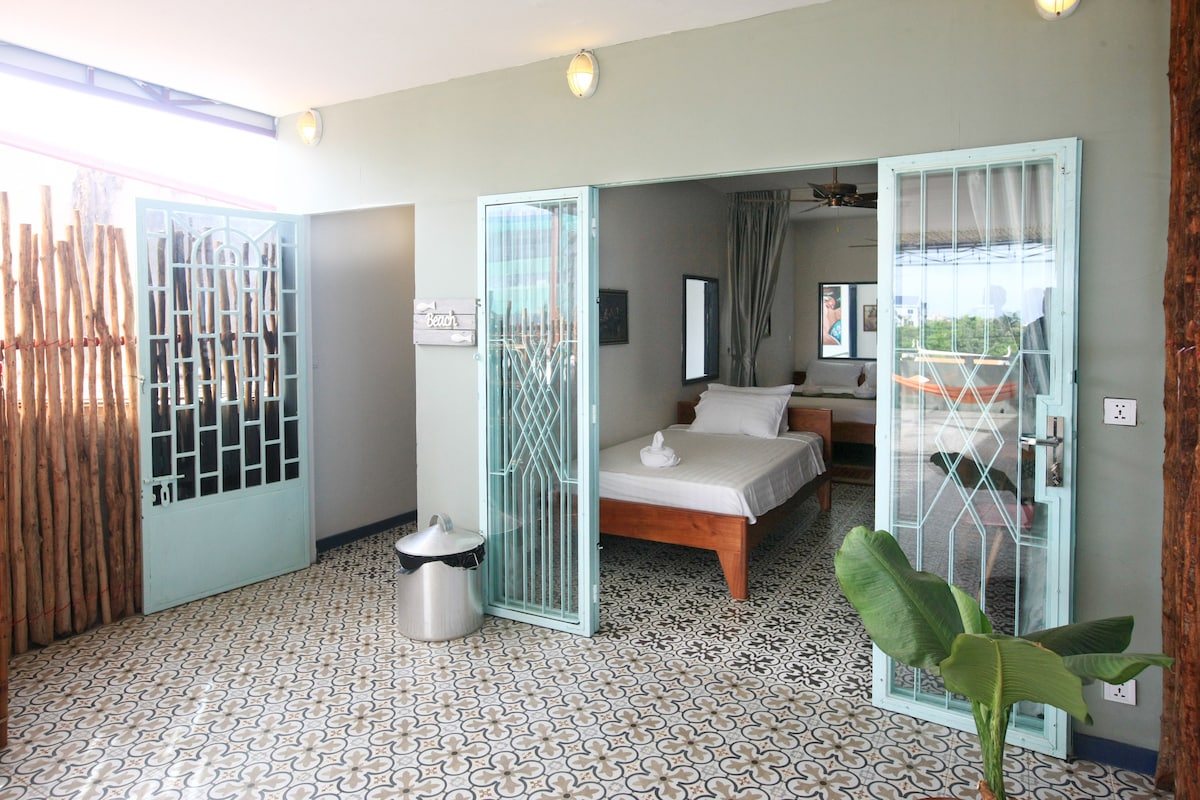 The entrance to a spacious bedroom is framed by double doors with intricate glass patterns. A light-colored wooden bed is visible inside, accompanied by soft linens. The floor boasts decorative tiles, and a potted plant adds a touch of greenery to the entrance.