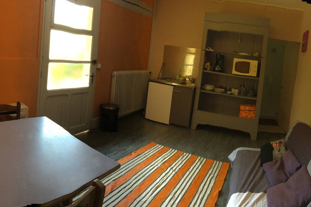 Pièce à vivre avec kitchenette , vaisselles , micro onde et cafetière ..une table , 2 chaises et un petit canapé .