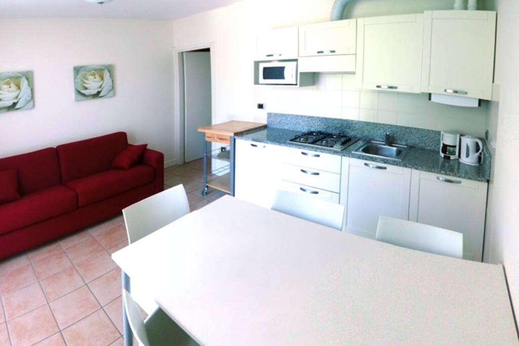 De 2 pers. slaapbank, deur naar bad- en slaapkamer. Keuken, met eettafel voor 4. Vanaf locatie van het TV scherm genomen.