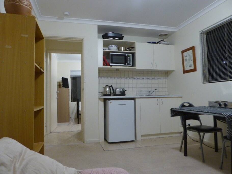 Living room with kitchenette, appliances, comfy couch, TV, table, shelving, microwave